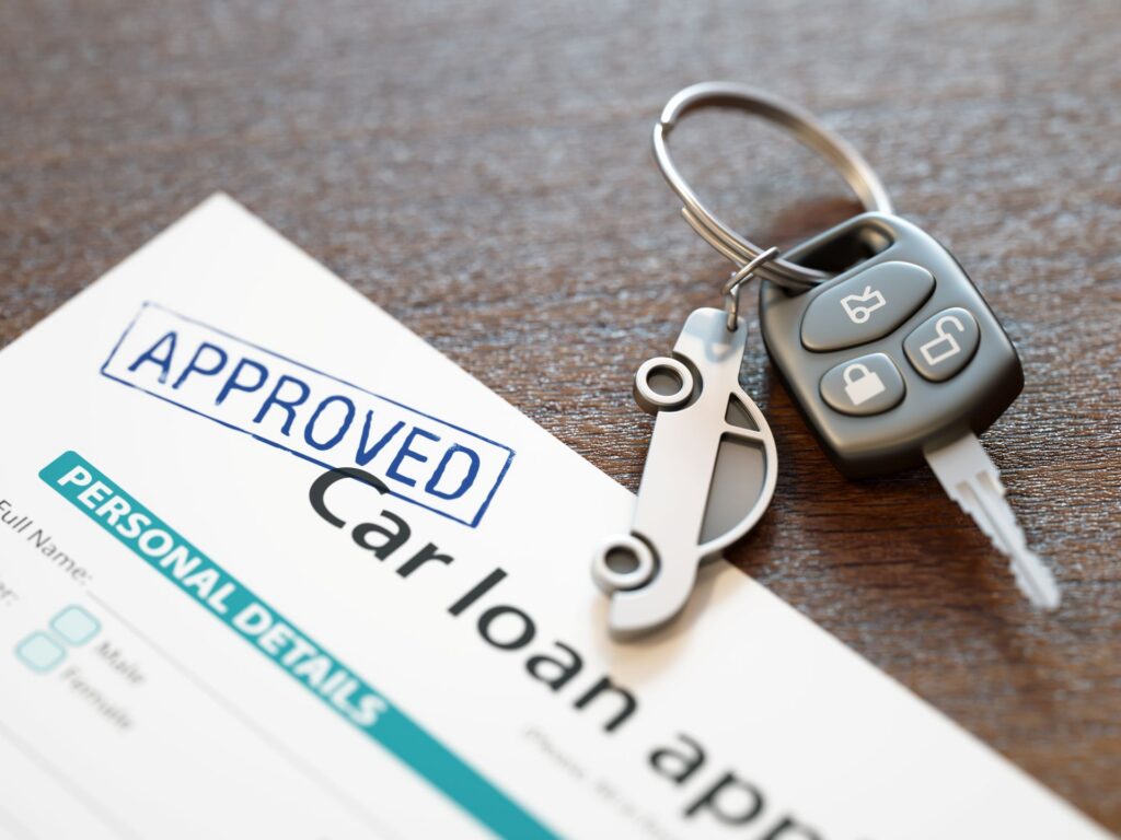 A set of keys with a car keychain next to car loan papers stamped with approved