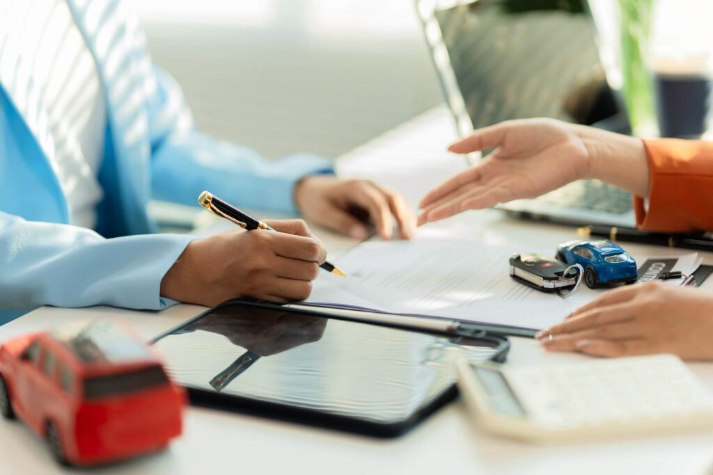 car loan approval in bright office with creditor signing loan paperwork beside laptop and toy cars.