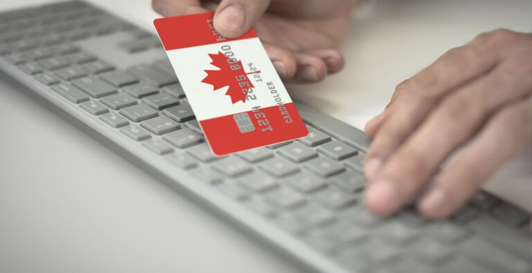 A newcomer to Canada holding a Canadian flag branded credit card over a keyboard.