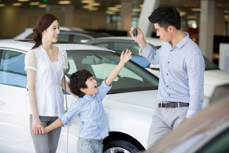 A family leaning on an open hatchback vehicle visiting a dealership with diverse background sales advisor helping them choose a model