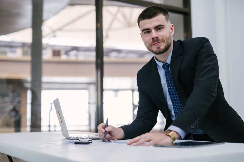Auto dealer sales advisor reaching out with keys beside laptop and model car.
